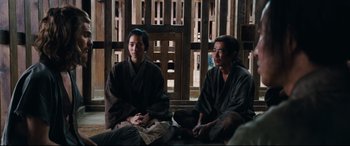 Movie still from “Silence” (2016), directed by Martin Scorsese – A man and a woman sitting on the ground in front of a building; Medium shot, Over the shoulder angle
