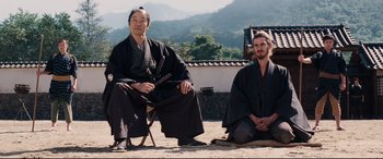 Movie still from “Silence” (2016), directed by Martin Scorsese – Two men sitting on the ground in front of a mountain; Medium shot, Low angle