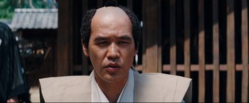 Movie still from “Silence” (2016), directed by Martin Scorsese – A man in a suit with a bald head; Close Up shot, Low angle