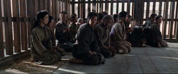 Movie still from “Silence” (2016), directed by Martin Scorsese – A group of people sitting on the ground in a room; Wide shot, High angle