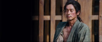 Movie still from “Silence” (2016), directed by Martin Scorsese – A man with long black hair wearing a green shirt; Medium shot, Low angle