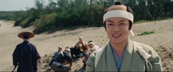 Movie still from “Silence” (2016), directed by Martin Scorsese – A group of people sitting on the beach with a man wearing a bandage on his head; Close Up shot, Low angle