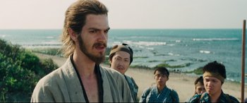 Movie still from “Silence” (2016), directed by Martin Scorsese – A group of men standing on top of a sandy beach; Close Up shot, Over the shoulder angle