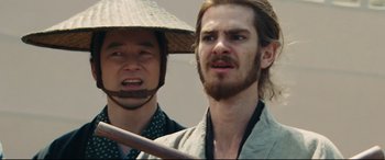 Movie still from “Silence” (2016), directed by Martin Scorsese – A man with long hair wearing a hat and holding a sword; Close Up shot, Low angle