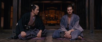 Movie still from “Silence” (2016), directed by Martin Scorsese – Two men sitting on the ground in front of a fireplace; Medium shot, Low angle