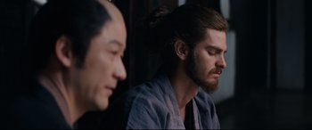 Movie still from “Silence” (2016), directed by Martin Scorsese – A man with long hair is sitting next to another man with long hair; Close Up shot, Over the shoulder angle