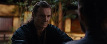 Movie still from “Silence” (2016), directed by Martin Scorsese – A man with long hair and a black robe is sitting outside; Close Up shot, Over the shoulder angle