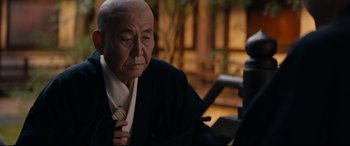 Movie still from “Silence” (2016), directed by Martin Scorsese – An older man sitting down with his hands on his chest; Close Up shot, Over the shoulder angle