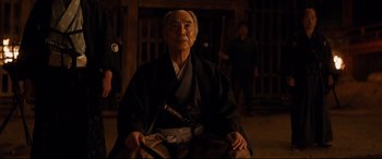 Movie still from “Silence” (2016), directed by Martin Scorsese – An old man sitting in a chair wearing a black robe; Medium shot, Over the shoulder angle