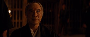 Movie still from “Silence” (2016), directed by Martin Scorsese – An older man wearing a black robe and a white shirt; Close Up shot, Low angle