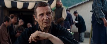 Movie still from “Silence” (2016), directed by Martin Scorsese – A man with long hair is sitting in front of other men; Close Up shot, Over the shoulder angle