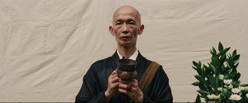 Movie still from “Silence” (2016), directed by Martin Scorsese – An older man holding a bowl in front of a white background; Close Up shot, Low angle