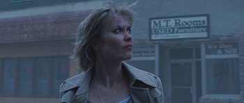 Movie still from “Silent Hill” (2006), directed by Christophe Gans – A woman in a trench coat standing in front of a building; Close Up shot, Low angle