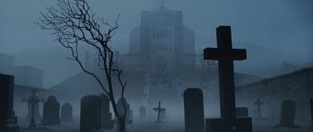 Movie still from “Silent Hill” (2006), directed by Christophe Gans – A graveyard with a cross and a building in the background; Extreme Wide shot, Low angle