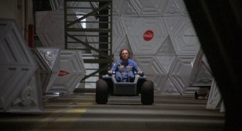 Movie still from “Silent Running” (1972), directed by Douglas Trumbull – A man sitting in a toy vehicle in a warehouse; Wide shot, High angle