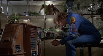 Movie still from “Silent Running” (1972), directed by Douglas Trumbull – A man in a blue shirt is kneeling in front of a desk; Medium shot, Low angle