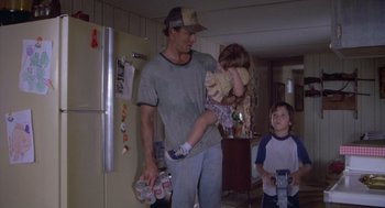 Movie still from “Silkwood” (1983), directed by Mike Nichols – A man holding a child in his arms while standing in a kitchen; Medium shot, Low angle