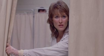 Movie still from “Silkwood” (1983), directed by Mike Nichols – A woman in a white shirt is leaning against a wall in a room; Close Up shot, Over the shoulder angle