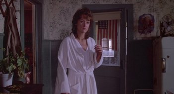 Movie still from “Silkwood” (1983), directed by Mike Nichols – A woman in a white robe holding an american flag sticker; Medium shot, Over the shoulder angle