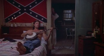 Movie still from “Silkwood” (1983), directed by Mike Nichols – A man sitting on a bed playing a banjo; Wide shot, Low angle