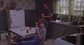 Movie still from “Silkwood” (1983), directed by Mike Nichols – A woman sitting at a table in front of a man in a kitchen; Medium shot, Over the shoulder angle