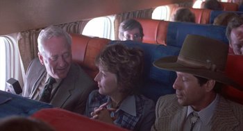 Movie still from “Silkwood” (1983), directed by Mike Nichols – A group of people sitting on a seat on an airplane; Medium shot, Over the shoulder angle