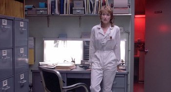 Movie still from “Silkwood” (1983), directed by Mike Nichols – A woman standing in front of a desk in a room; Medium shot, Low angle