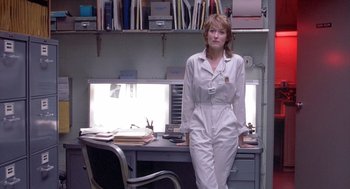 Movie still from “Silkwood” (1983), directed by Mike Nichols – A woman standing in front of a desk in a room; Medium shot, Low angle