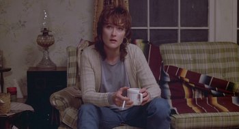 Movie still from “Silkwood” (1983), directed by Mike Nichols – A woman sitting on top of a couch holding a coffee mug; Medium shot, High angle
