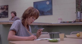 Movie still from “Silkwood” (1983), directed by Mike Nichols – A woman sitting at a table writing on a piece of paper; Medium shot, Over the shoulder angle