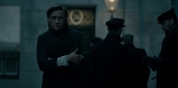 Movie still from “A Fortunate Man” (2018), directed by Bille August – A man standing in the dark with his arms crossed; Medium shot, Low angle