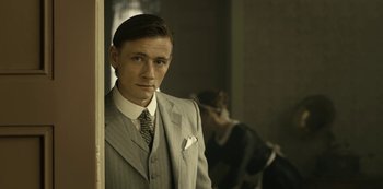 Movie still from “A Fortunate Man” (2018), directed by Bille August – A man in a suit and tie standing in front of a mirror; Medium shot, Low angle