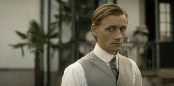 Movie still from “A Fortunate Man” (2018), directed by Bille August – A man wearing a suit and tie standing in front of a building; Close Up shot, Low angle
