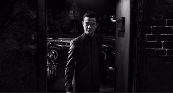 Movie still from “Sin City: A Dame to Kill For” (2014), directed by Frank Miller – A black and white photo of a man in a suit; Medium shot, Low angle