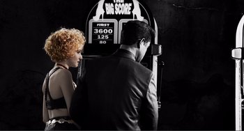 Movie still from “Sin City: A Dame to Kill For” (2014), directed by Frank Miller – A man and a woman standing next to each other in front of an arcade machine; Medium shot, Low angle