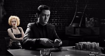 Movie still from “Sin City: A Dame to Kill For” (2014), directed by Frank Miller – Black and white photograph of a man sitting at a table; Medium shot, Low angle