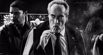 Movie still from “Sin City: A Dame to Kill For” (2014), directed by Frank Miller – An older man smoking a cigarette in a suit and tie; Close Up shot, Low angle