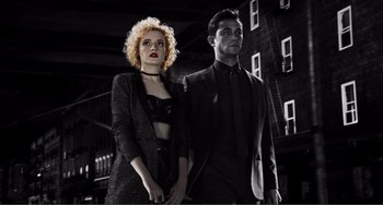 Movie still from “Sin City: A Dame to Kill For” (2014), directed by Frank Miller – A man and a woman standing next to each other in front of a building; Medium shot, Low angle