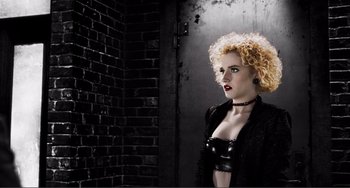 Movie still from “Sin City: A Dame to Kill For” (2014), directed by Frank Miller – A woman with blonde curly hair wearing a black jacket; Medium shot, Low angle