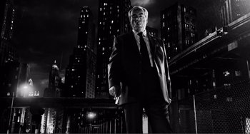 Movie still from “Sin City: A Dame to Kill For” (2014), directed by Frank Miller – A man in a suit and tie standing in front of buildings; Medium shot, Low angle