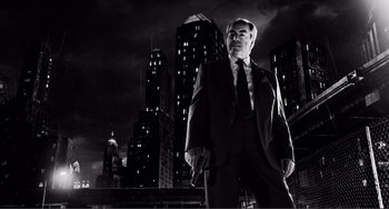 Movie still from “Sin City: A Dame to Kill For” (2014), directed by Frank Miller – Black and white photograph of a man in a suit in a city at night; Medium shot, Low angle
