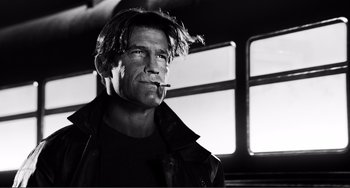 Movie still from “Sin City: A Dame to Kill For” (2014), directed by Frank Miller – Black and white photograph of a man smoking a cigarette in front of a bus; Close Up shot, Low angle