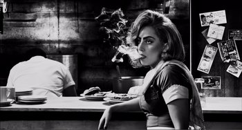 Movie still from “Sin City: A Dame to Kill For” (2014), directed by Frank Miller – A woman sitting at a table smoking a cigarette; Medium shot, Low angle