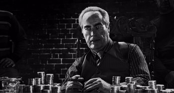 Movie still from “Sin City: A Dame to Kill For” (2014), directed by Frank Miller – An older man sitting in front of stacks of coins; Close Up shot, Low angle