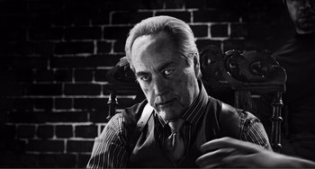 Movie still from “Sin City: A Dame to Kill For” (2014), directed by Frank Miller – An older man sitting in a chair in front of a brick wall; Close Up shot, Low angle