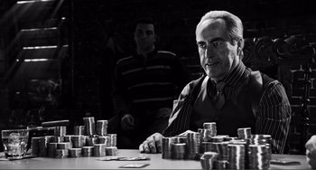 Movie still from “Sin City: A Dame to Kill For” (2014), directed by Frank Miller – A man sitting at a table with stacks of coins in front of him; Medium shot, Over the shoulder angle