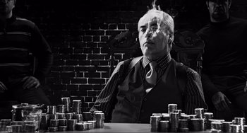 Movie still from “Sin City: A Dame to Kill For” (2014), directed by Frank Miller – An older man sitting in front of stacks of coins; Medium shot, Low angle