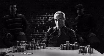 Movie still from “Sin City: A Dame to Kill For” (2014), directed by Frank Miller – A man sitting at a table in front of stacks of coins; Medium shot, Over the shoulder angle