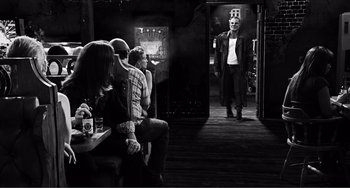 Movie still from “Sin City: A Dame to Kill For” (2014), directed by Frank Miller – A group of people sitting in front of a man in a room; Wide shot, Over the shoulder angle