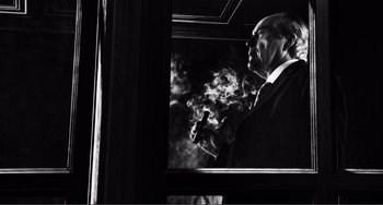 Movie still from “Sin City: A Dame to Kill For” (2014), directed by Frank Miller – A black and white photo of a man smoking a cigarette; Medium shot, Low angle